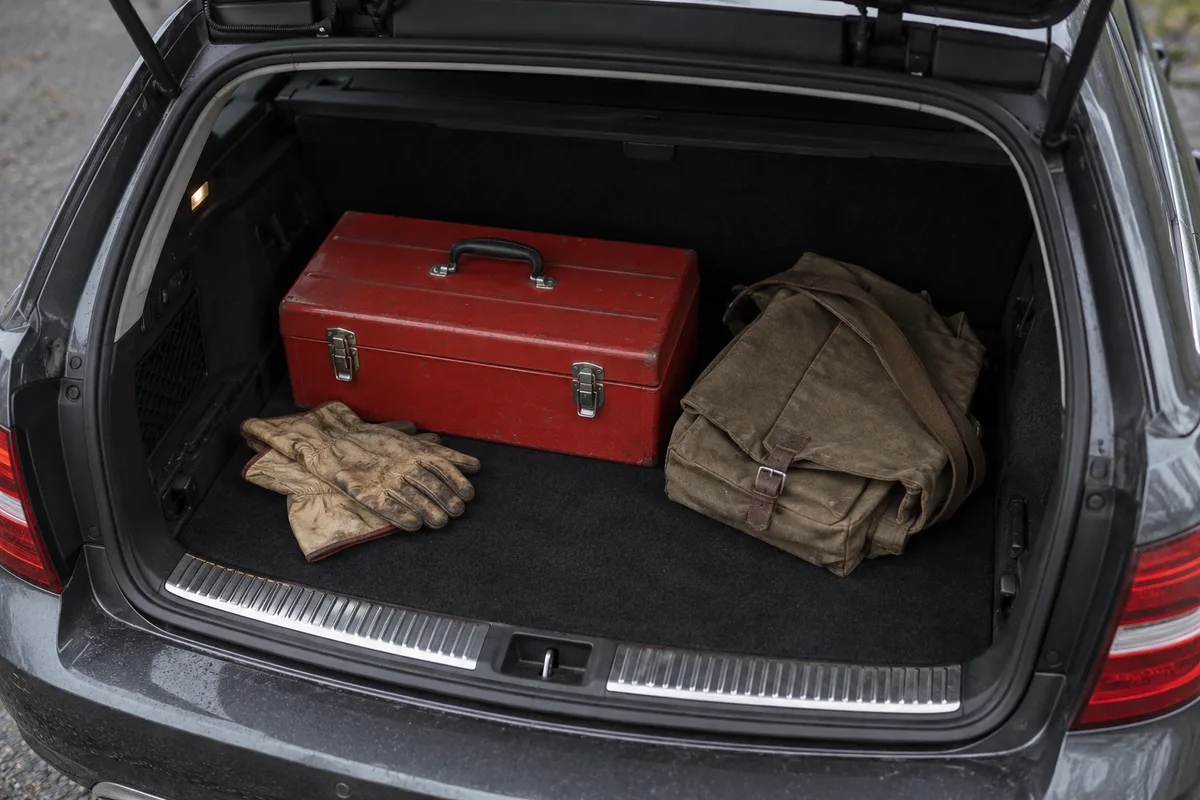 Coffre ouvert d’une voiture break avec une caisse à outils fermée et des gants de travail